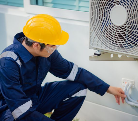 Male technician checking a cooling pipeline of the air conditioner outdoors.